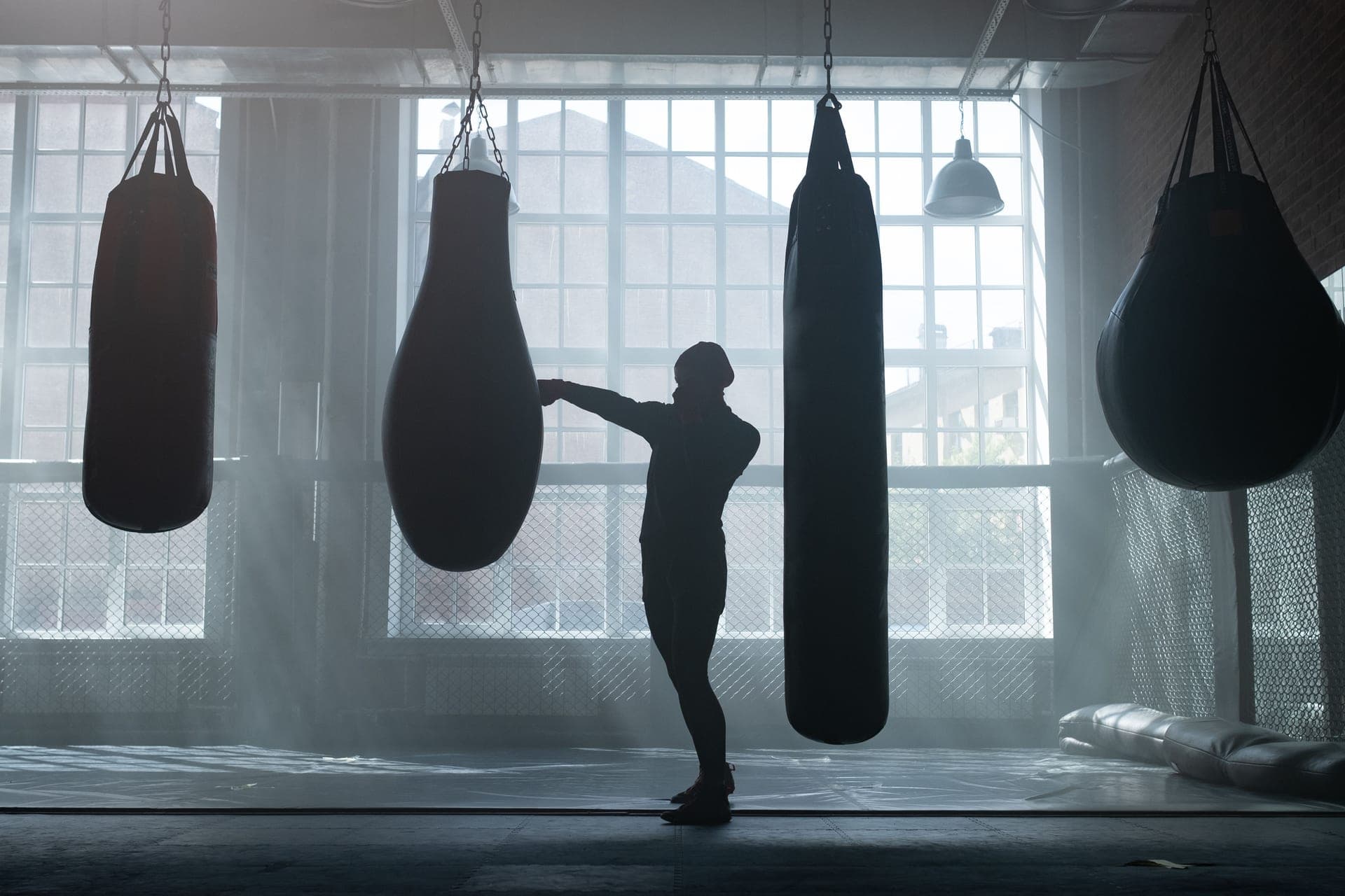 A person training on heavy bags in an industrial-style boxing gym with large windows