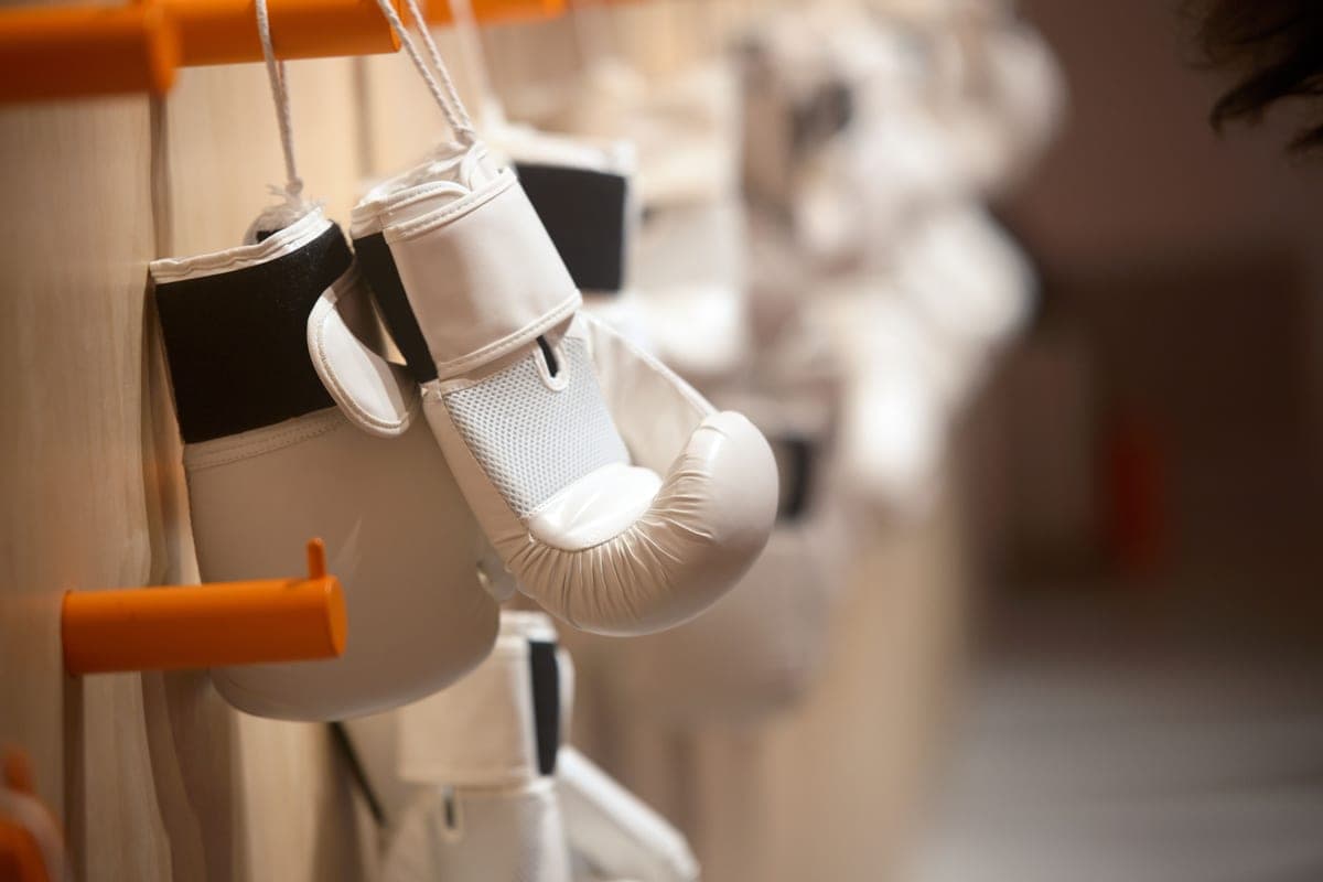 White hook-and-loop boxing gloves hanging on a hook in a gym