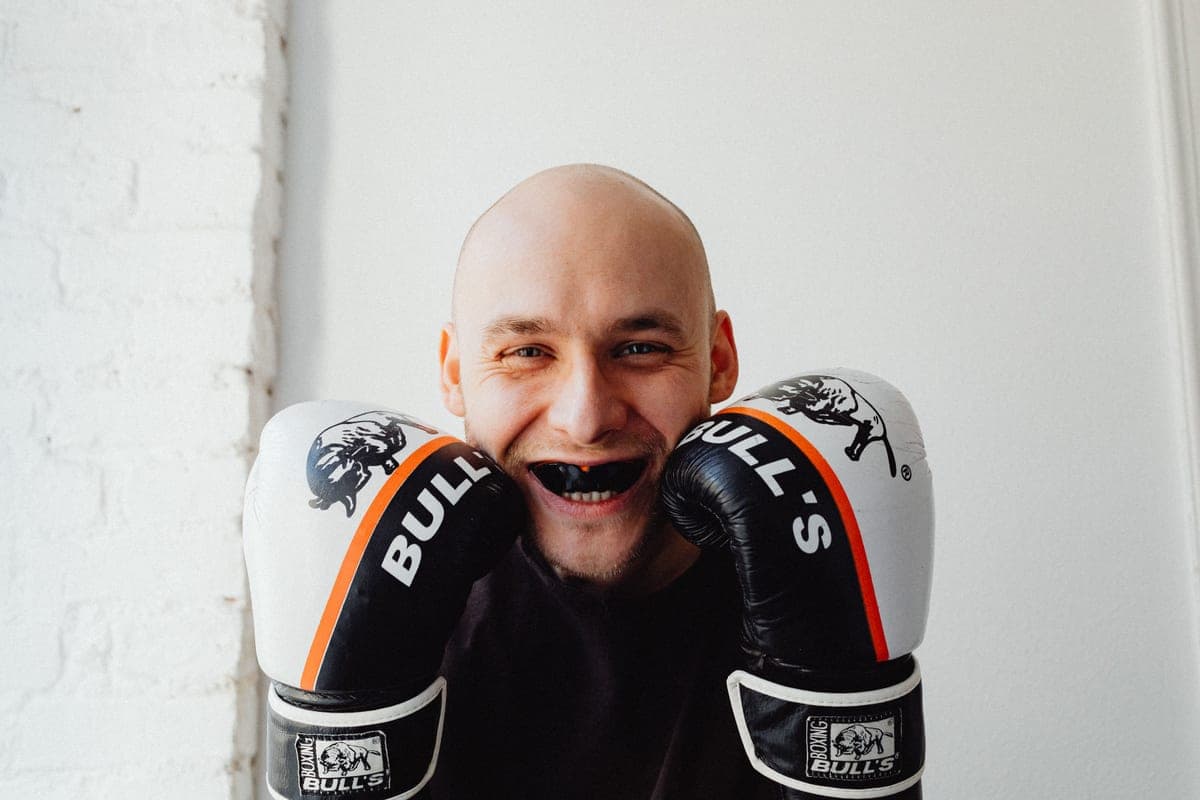 A smiling boxer wearing gloves and a mouthguard indoors
